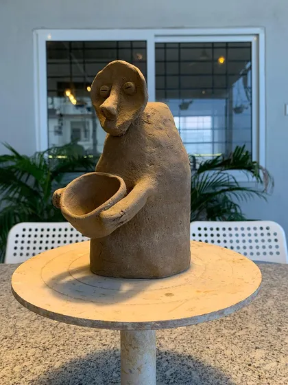 A primitive, expressive sculpture of a figure holding a bowl. This piece has a raw, powerful energy.