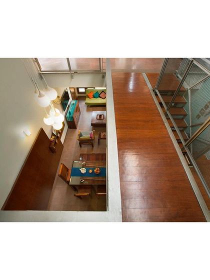 A view from the upper bridge looking down into the open-plan living and dining area of the Interlocking House. The double-height cutout visually connects the two floors, enhancing the sense of volume and shared space within the home.