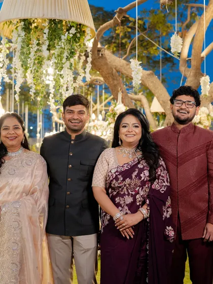 A family portrait from a pre-wedding reception. The brother of the bride (far right) wears a deep maroon bandhgala, a sophisticated choice that coordinates with the family's jewel-toned color palette.