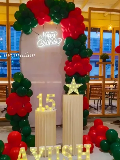 A bold red and green themed 15th birthday party. The decor features a balloon arch, a neon sign, and light-up marquee numbers and name.