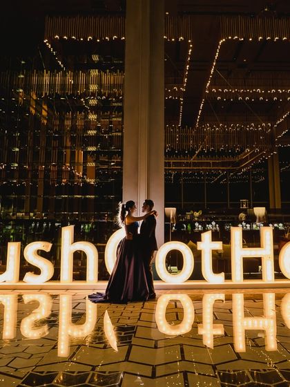 A couple poses in front of a large, illuminated sign with their wedding hashtag. This kind of personalized branding is a key element in our themed events.