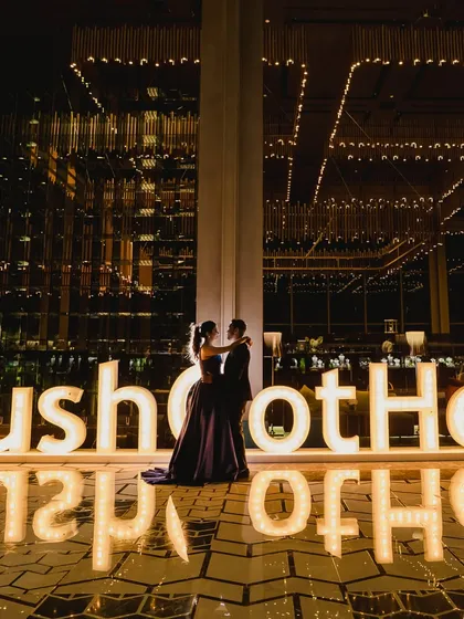 A couple poses in front of a large, illuminated sign with their wedding hashtag. This kind of personalized branding is a key element in our themed events.