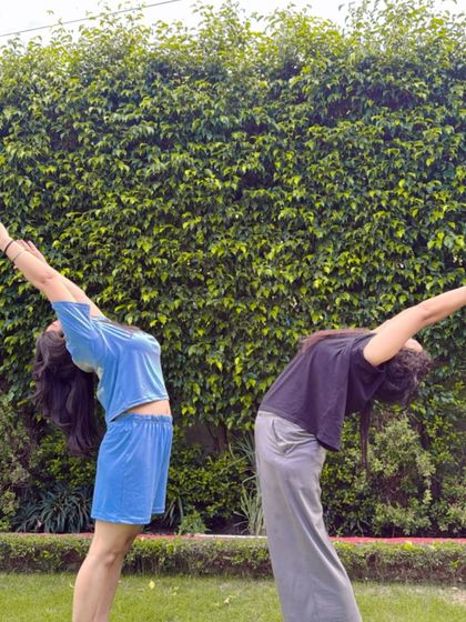 A partner backbend in the park, surrounded by greenery.
