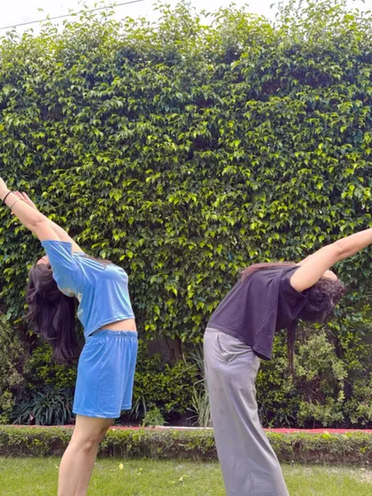 A partner backbend in the park, surrounded by greenery.