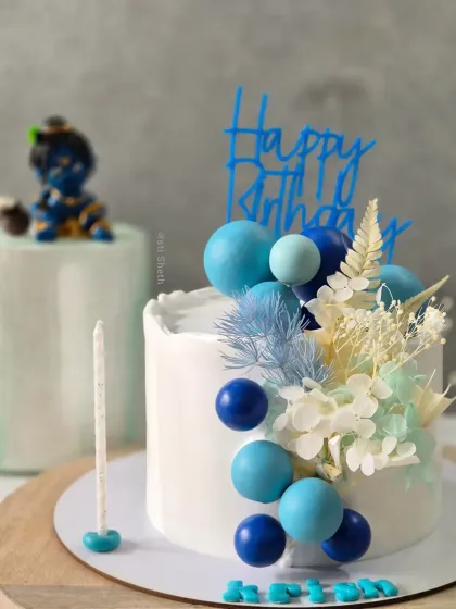 A beautiful cake for Janmashtami, decorated in shades of blue with dried florals and a small Krishna topper in the background.