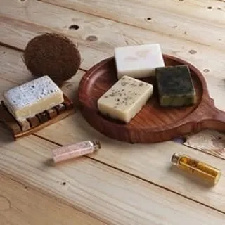 A lifestyle flat lay of various handmade soaps and beauty oils on a wooden platter, conveying a natural, organic aesthetic for a skincare brand.