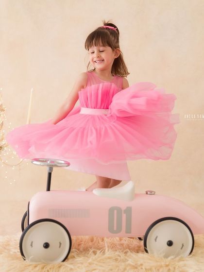 A playful moment as a little girl in a pink dress twirls and plays with her toy car in the studio.
