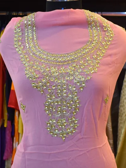 This pink suit features an elaborate, handcrafted neckline. This is an example of how we can customize a design based on a client's vision, turning a simple outfit into a statement piece.