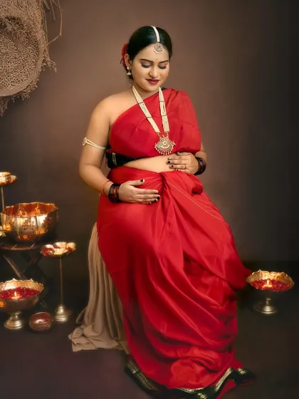 Seated amidst traditional brass lamps, this mother-to-be looks down at her bump with love, creating a peaceful and heartfelt image.