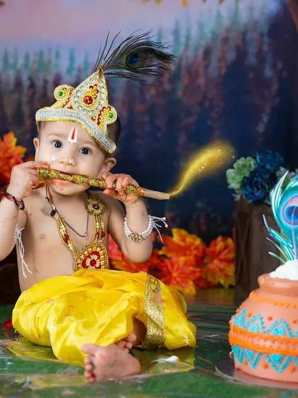 Enjoying a taste of his flute during his Krishna-themed birthday shoot. The forest backdrop and "ONE" blocks mark this special milestone.