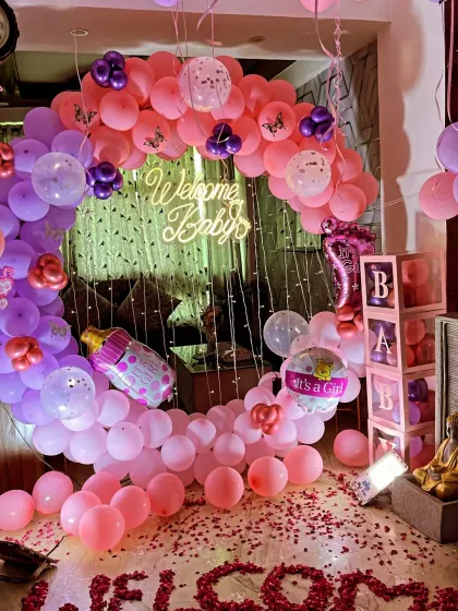 A clear shot of the 'Welcome Baby' ring backdrop, decorated with pink and purple balloons, baby-themed foil balloons, and a 'WELCOME' message made of rose petals.