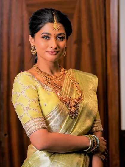 A portrait of the client in her light green saree, showcasing the beautiful fit of her custom blouse and how it complements her traditional gold jewelry.