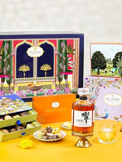 An assortment of beautifully packaged ITC Hotels Diwali gift boxes alongside a bottle of Hibiki whisky. This shot showcases a range of premium gifting options in a festive setting.