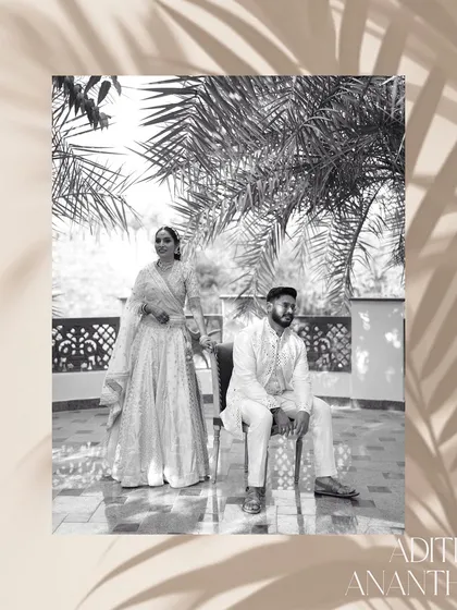 A timeless black and white portrait with an artistic, editorial feel. The couple is framed by palm leaves, creating a classic and sophisticated composition that emphasizes their elegant traditional attire.