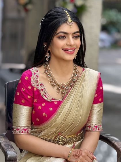 This bride's look for her event features a bright pink blouse and a cream saree. The makeup is soft and pretty, with a half-up hairstyle.