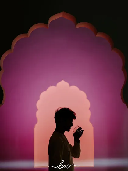 A creative silhouette of the groom, framed perfectly within a series of colorful Rajasthani arches, holding a drink.