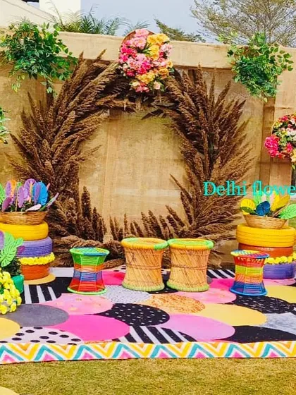 A rustic and colorful photo booth area for a Haldi carnival, using a jute backdrop, a wreath of dried wheat, and vibrant seating.