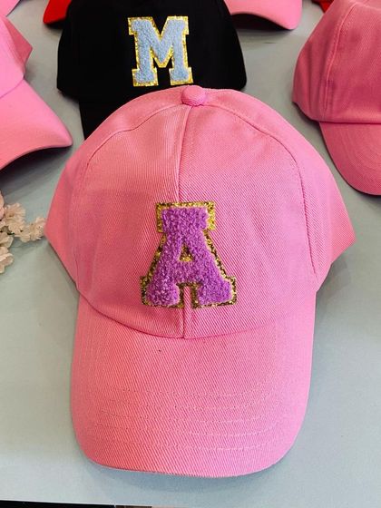 A close up of a pretty pink cap customized with a purple and gold glitter chenille 'A' patch. We focus on quality details to make each personalized gift special.