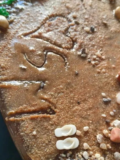 A detailed shot of the initials carved into the sand on the heart-shaped ocean art piece.