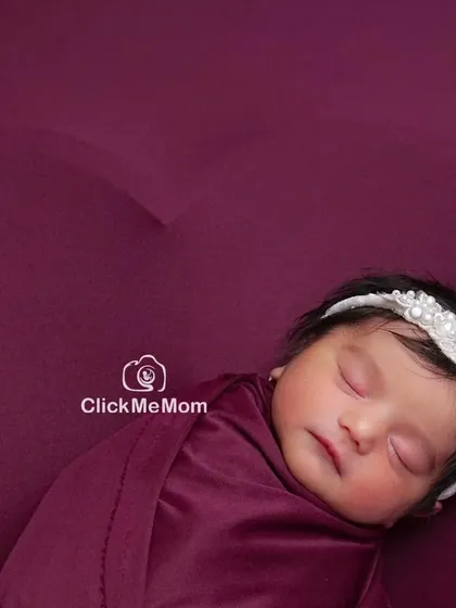 A simple and elegant portrait using a rich burgundy color for the swaddle and background, highlighting the baby's delicate features.
