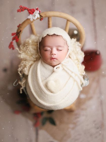Newborn bliss for the holidays. This six-week-old looks angelic in a cream wrap and bonnet, with subtle Christmas decorations for a festive touch.