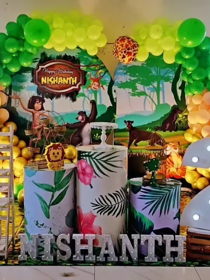 A Jungle Book themed birthday party with a vibrant backdrop showing Mowgli and Baloo. The setup is decorated with tropical leaf-printed pedestals and a large marquee number '2'.