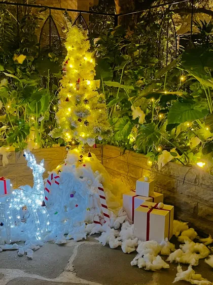 An enchanting outdoor Christmas installation perfect for a corporate building entrance or garden. This setup includes a beautifully lit white Christmas tree, glowing reindeer figures, faux snow, and neatly wrapped gift box props, creating a magical winter wonderland scene.