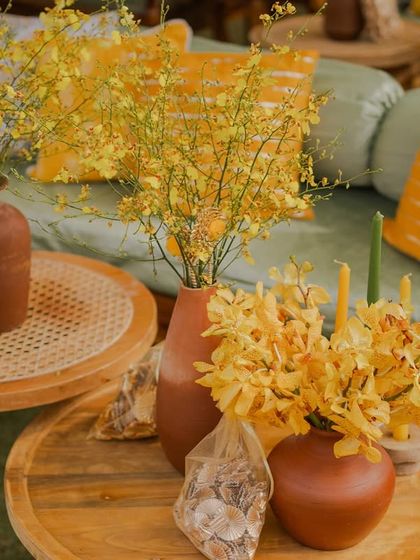 A tabletop arrangement of terracotta vases filled with yellow orchids and other blooms, adding to the 'Bageecha' theme.