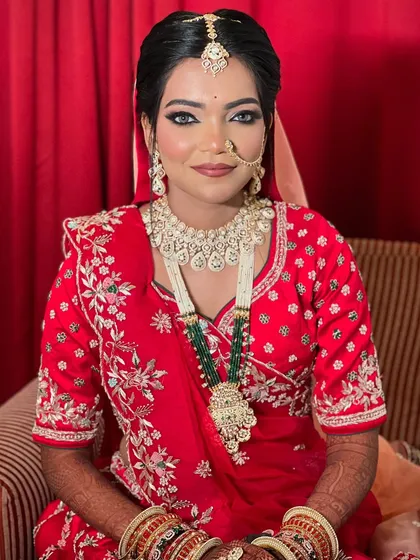 A full portrait of the bride seated, looking regal in her red lehenga and heavy jewellery.
