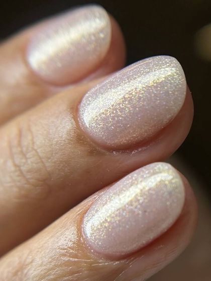 A close-up of a beautiful, light-colored cat-eye manicure. The golden magnetic shimmer creates a stunning band of light across the pearlescent base.
