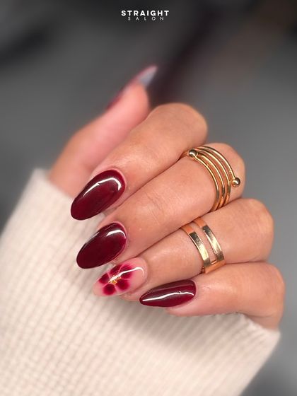 A deep burgundy manicure with a beautiful, hand-painted floral accent nail. The soft, blended petals create a stunning contrast against the dark base.