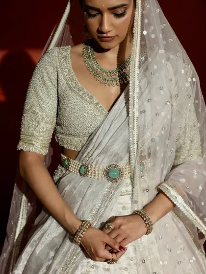 A detailed view of the couture craftsmanship, this shot highlights the exquisite hand-embroidery on the bridal blouse. The precise pearl work, sweetheart neckline, and the unique emerald-studded belt demonstrate the level of artistry that goes into each bespoke creation.