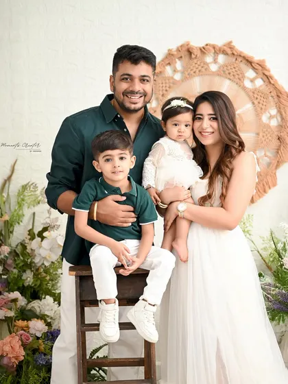 A lovely family portrait showcasing the bond between siblings. The older brother sits proudly next to his baby sister, held by their loving parents.
