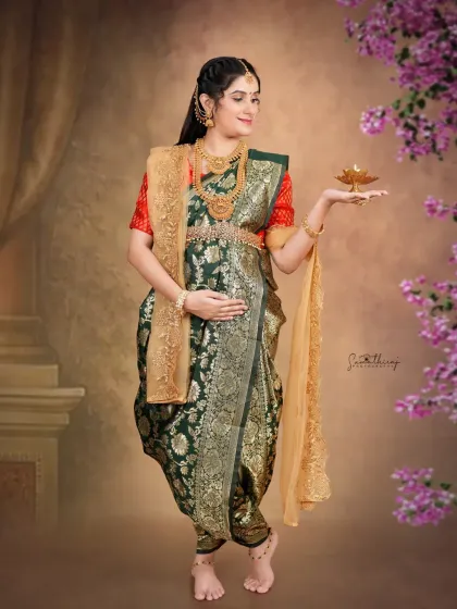A full-length portrait of a mother-to-be holding a diya, dressed in a traditional green saree. The floral elements and serene pose create a beautiful and symbolic image.
