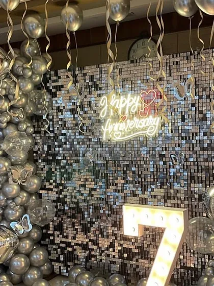 A glamorous 7th-anniversary celebration with a silver sequin shimmer wall. I framed it with a silver chrome balloon arch, added butterfly details, and hung more balloons from the ceiling to create a sparkling, festive atmosphere.