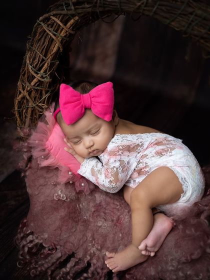 A side-on view of the baby sleeping, showing off the delicate lace outfit and the big pink bow.