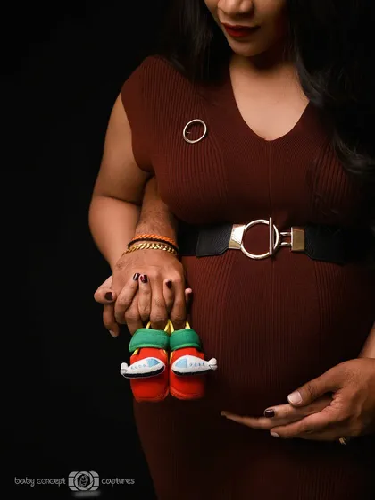 A creative close-up shot focusing on the baby bump. The couple's hands are intertwined, holding a tiny pair of baby shoes, symbolizing their shared anticipation and love for their little one.