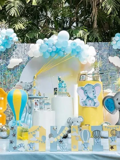 A cheerful and adorable baby elephant theme for a third birthday. The pastel blue and yellow color scheme, complete with a large marquee number and hot air balloon prop, creates a playful and sunny vibe.