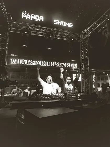 A classic black and white photo from the DJ booth, with both me and my partner raising our hands with the crowd. It's a timeless image of unity and celebration.