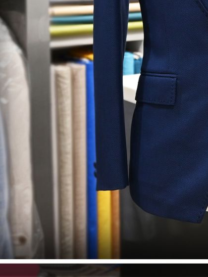A close-up detail shot of the blue suit's sleeve and pocket, showcasing the quality of the fabric and tailoring.