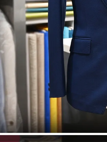 A detailed side view of the blue tuxedo jacket, with rolls of fabric visible in the background.