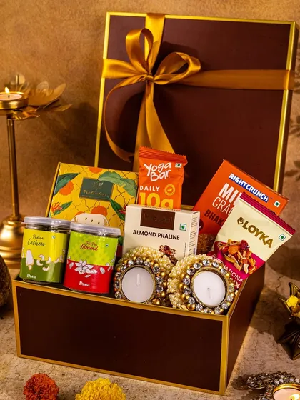This shot focuses on a rich brown and gold hamper, creating a sense of warmth and luxury. The arrangement of snacks and diyas around the box makes it feel like a complete festive offering.