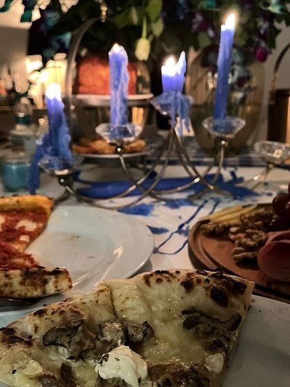 An atmospheric shot of a dinner party table set with glowing candles. Slices of my mushroom and Margherita pizza sit alongside a grazing board, creating an intimate and inviting dining experience.