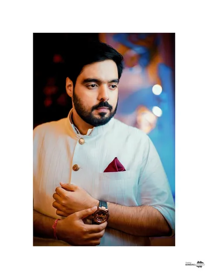 A handsome portrait of the groom, looking thoughtful and stylish. The simple white kurta and the pop of color from his pocket square create a modern and elegant look.