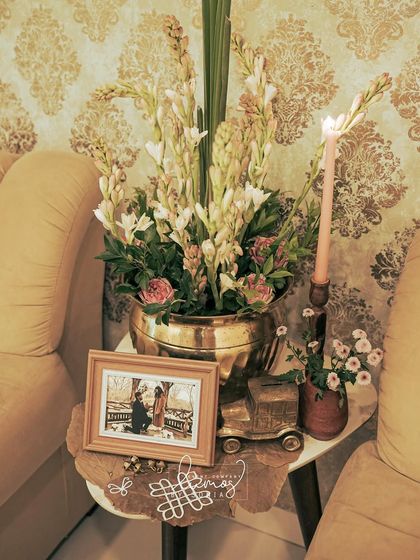 A beautiful arrangement of tuberoses and other flowers in a brass vase, placed next to a vintage car model and a framed photo.