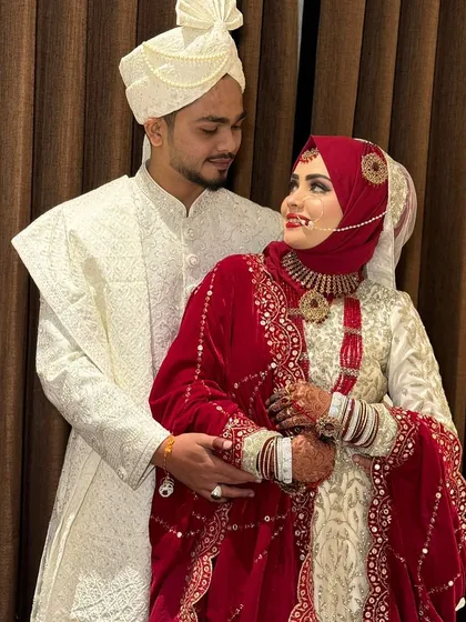 A beautiful portrait of the royal Hijabi bride and her groom. Her makeup, featuring a classic red lip and defined eyes, looks stunning next to her husband's elegant white sherwani.