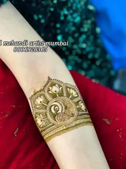 A close-up of a beautifully detailed arm band. The design includes a peacock surrounded by lotus flowers, showcasing clean lines and precise shading.