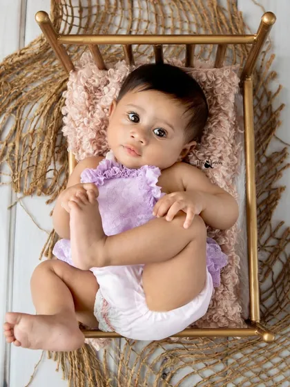 A beautiful overhead shot of a baby girl lying on a miniature bed. Sitter sessions are perfect for capturing babies once they can lie on their back and play with their feet.