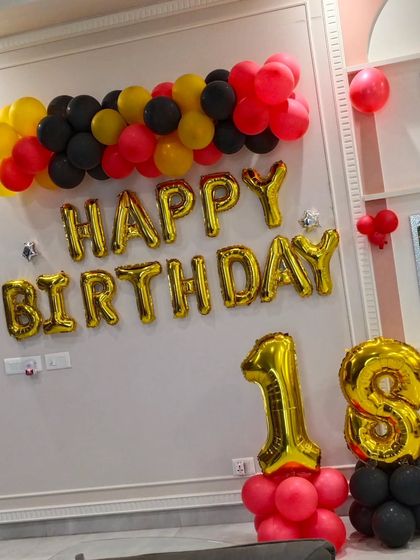 Celebrating an 18th birthday with a bold color scheme. This wall decoration uses red, yellow, and black balloons with large gold foil letters and numbers to mark the special occasion.