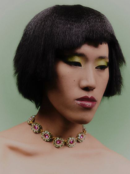 A beauty portrait focused on a stunning, multi-colored gemstone necklace. The model's minimal styling and bold green eyeshadow make the jewelry pop.